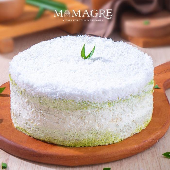 Putu Pandan Cake bulat utuh berbalut kelapa parut di atas piring kayu.